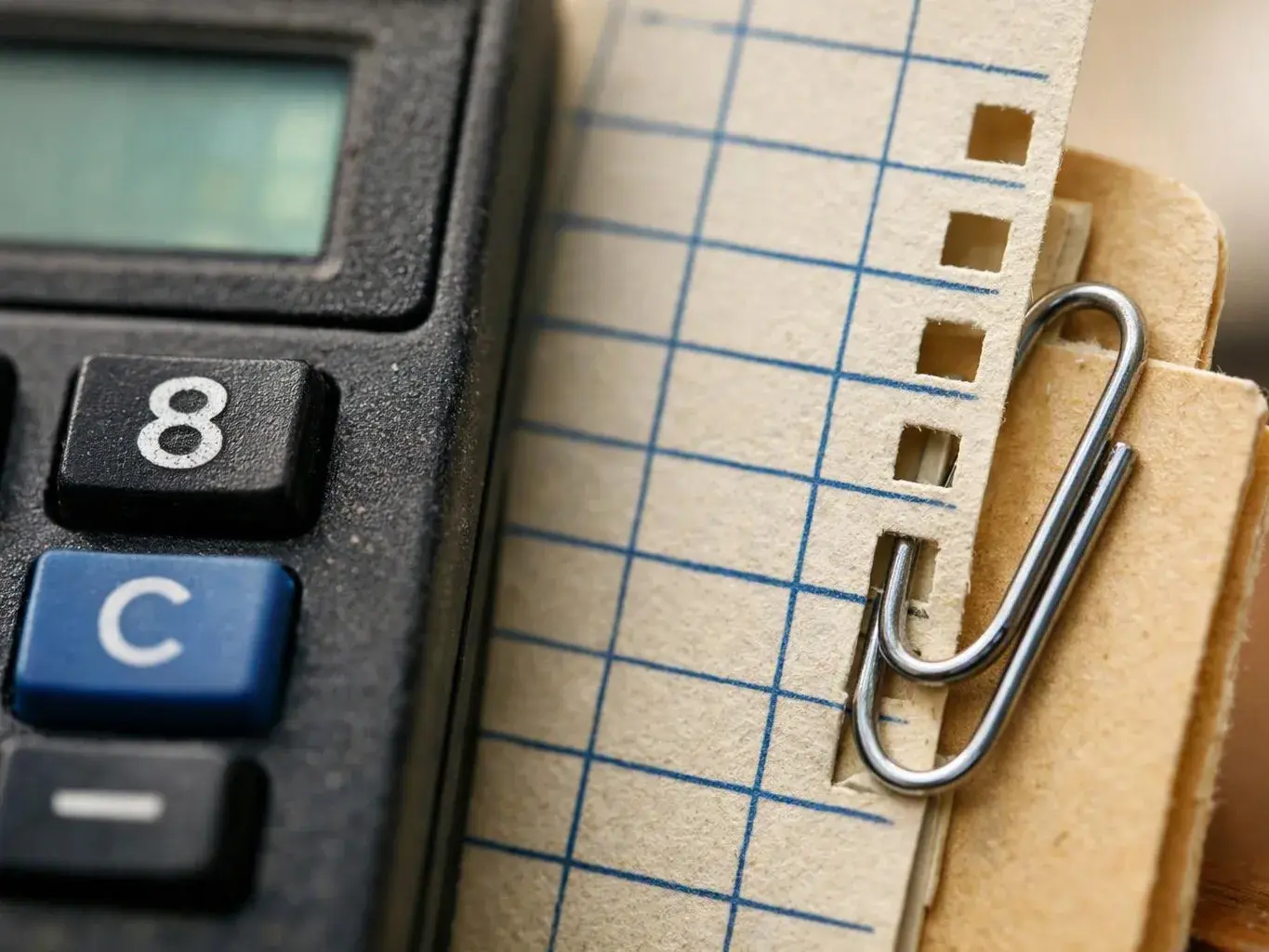 Close-up of a calculator beside graph paper and a paperclip clipped to a file folder